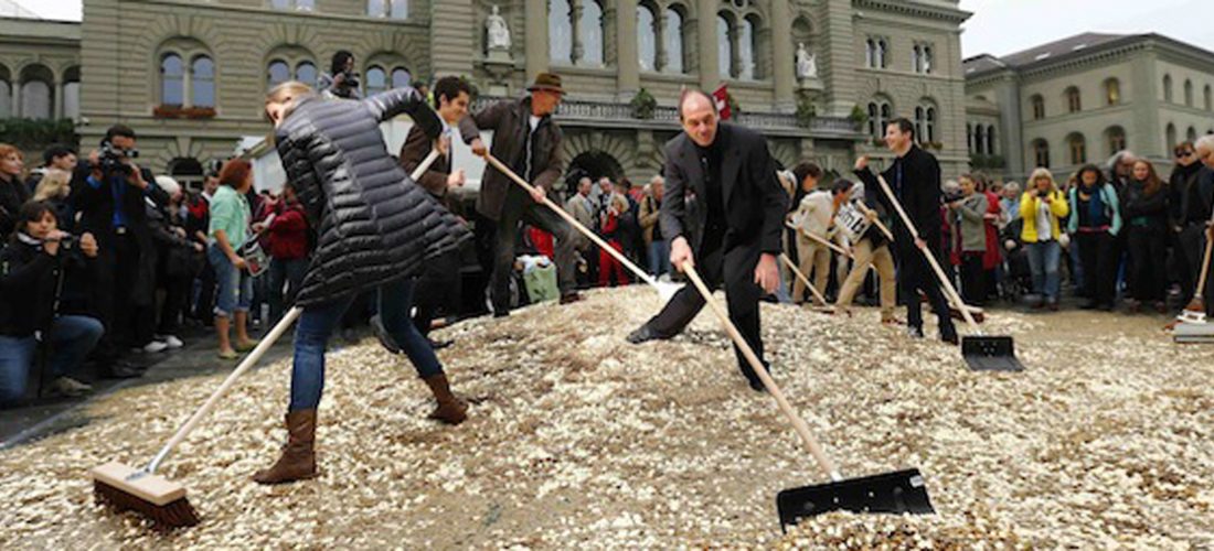 Committee members use brooms and shovels to spread out five cent coins over the Federal Square during an event organised by the Committee for the initiative "CHF 2,500 monthly for everyone" (Grundeinkommen) in Bern October 4, 2013. The Committee delivered 126,000 signatures to the Chancellery on Friday to propose a change in the constitution to implement their initiative. The initiative aims to have a minimum monthly disposal household income of CHF 2,500 (US$ 2,700) given by the government to every citizen living in Switzerland. REUTERS/Denis Balibouse (SWITZERLAND - Tags: POLITICS CIVIL UNREST)